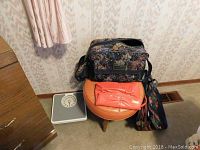 Photo showing the wood and plastic covered stool with orange seat, three carry-on bags, and the analog bathroom scale positioned on the floor.
