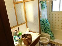 Bathroom countertop showing personal care bottles, curling iron, and woven waste basket placed on counter next to sink and toilet.