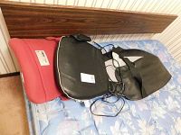 Two back support items lying on a bed: a red ObusForme back rest and a black HoMedics shiatsu massage cushion with wired remote.