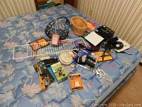 Wide view of various household and garden items on a bed including metal basket, wooden basket, scissors, camera case, brushes, and other small tools for sale