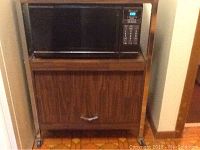 Full view of Kenmore microwave oven placed on top of wooden stand with cabinet below.