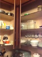 Two cupboards featuring various dishes, mugs, and plastic storage containers arranged on shelves.