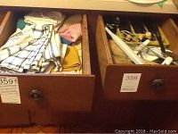 Two wooden drawers containing assorted hand towels, flatware, and kitchen utensils.