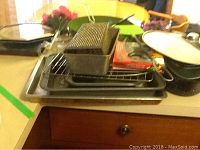Full lot view showing stacked baking trays, wire rack, metal grater, metal container, boxed quartz clock, and black pot with white lid.