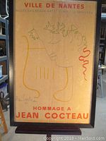 Full view of framed vintage poster titled "Hommage a Jean Cocteau" with visible text and art design, showing signature.