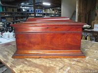 Left side view of closed mahogany music box case on wooden table.