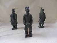 Front view of three vintage black Chinese warrior figurines standing on integral square bases, each holding a gold blade halberd.