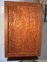 Full view of framed wooden relief showing temple village scene with figures and trees