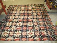 Full view of the antique two panel wool coverlet showing its medallion pattern in coral pink, black, white, and brown colors spread on floor.