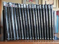 Full view of 18 black-spined hardcover books with monochrome historic portraits on top section, titles printed in gold text along spine, arranged upright.