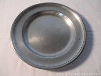 Full view of the antique pewter plate showing the round shape, raised rim, and overall finish.