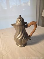 Front and side view of antique pewter tea pot with wooden handle showing fluted body and spout.