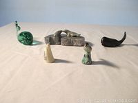 Wide shot of the five miniature figurines including the green glass whale, stone sea lions, two carved whales, and painted songbird.