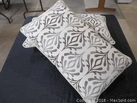 Two rectangular Ethan Allen pillows with geometric leaf pattern stacked on black fabric surface.
