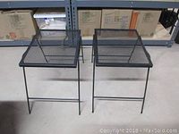 Two black metal mesh patio tables with folding legs, shown from the front shot.
