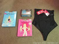 Four new Spanx garments in original packaging and one out of packaging displayed on floor.