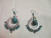 Front view of pair of silver-tone hoop earrings with turquoise beads and dangling small silver charms.