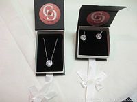 Photo of boxed necklace and matching earrings showing set in presentation boxes with brand logo.