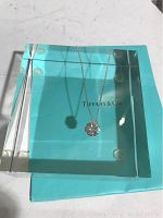 Tiffany & Co. Crown of Hearts sterling silver pendant displayed on transparent acrylic block above Tiffany blue pouch.