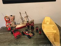 Overview of lots showing Amish figurines, wooden boats, Japanese litho vehicles, and plush dolls arranged on a wooden table.