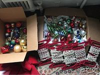 Overview photo showing cardboard box filled with mixed glass ornaments in varied shapes and colors, red garland holders, and pearl garlands.