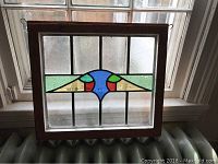 Front view of stained glass window panel showing colored abstract design within textured leaded glass and wooden frame, hanging on a window.