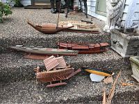 Multiple vintage model boats disassembled or damaged, placed on concrete steps outdoors