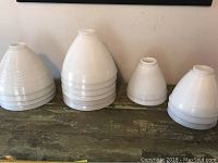 Photo showing all 15 vintage milk glass lampshades grouped by size, stacked on table.