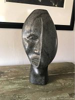 Front view of large carved stone primitive head sculpture showing detailed facial carving and polished finish