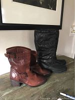 Two pairs of ladies boots placed side by side on a table, one brown leather ankle boot pair and one black winter boot pair with Coach logos.