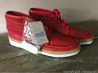 Side and front angle showing side profile of new red Adidas David Beckham sneakers with tags and white extra laces attached.