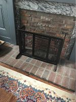 Front view of black metal fireplace screen with mesh and decorative scrolls against brick fireplace.