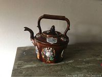 Front view of the brown glazed antique English barge ware teapot with floral decorations and inscription plaque.