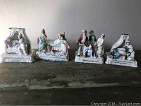 Four antique Victorian porcelain fairings arranged in a row on a wooden surface showing various domestic scenes and captions on their bases.