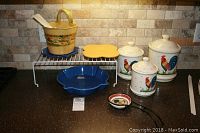 Wide view of ceramic kitchen items including trivets, pot with utensils, canisters, spoon rest, and dish on countertop