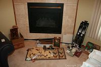 Wide shot showing multiple items spread on floor including curtain rods, valances, rugs, decorative box, and other items near fireplace.