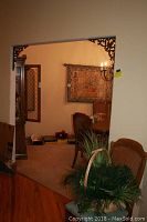 Photo showing interior doorway with a basket of faux greenery on chair seat and elements of wall art visible inside adjacent room.