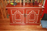 Front view of a solid wood entry cabinet showing two carved doors with floral and geometric patterns, metal handles at center and black knob latches at the sides.