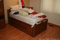 Full view of the twin solid wood bed frame with mattress on top, showing three large under-bed storage drawers on one side of the bed.