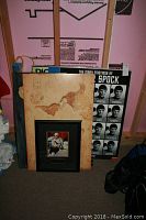 Photo of multiple framed wall art pieces including a vintage world map poster, the Many Emotions of Spock poster, and a framed Ron Francis hockey photo leaning against a wooden frame construction area