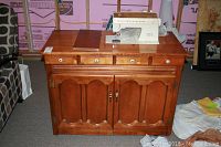 Front view of the solid maple cabinet with closed top, showing drawer knobs and door handles, with sewing machine closed inside.