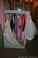 Foldable travel wardrobe with costumes visible on hangers inside, showing various colors and fabrics including pinks and whites with some tulle skirts.
