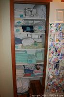 Linen closet with multiple shelves containing folded bedding and towels including mattress pads, sheet sets, duvets, pillowcases and towels.