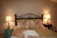 Pair of brass lamps lighting a bedroom, sitting on bedside tables next to a bed with floral bedding and multiple pillows.