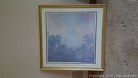 Framed print of Monet painting showing a soft impressionist landscape with trees and sky in a gold frame.