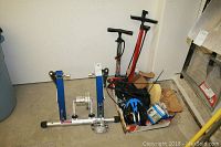 Full view of blue 1up USA bike trainer, two air pumps, and box of bicycle accessories including helmet, tubes, and seat.