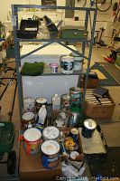 Photo shows gray metal shelving unit with multiple paint cans and supplies arranged on and near lower shelves.