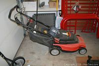 Side view of Black & Decker cordless lawn mower with red deck and catcher bag attached, folded handle.
