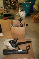 Toro Super Blower Vac with nozzle attachment and catcher bag lying on cardboard and cardboard box nearby.