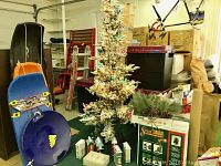 Full view of the flocked and lit Christmas tree surrounded by Hallmark tin sweet boxes and holiday decor pieces, including pine cones and greenery.